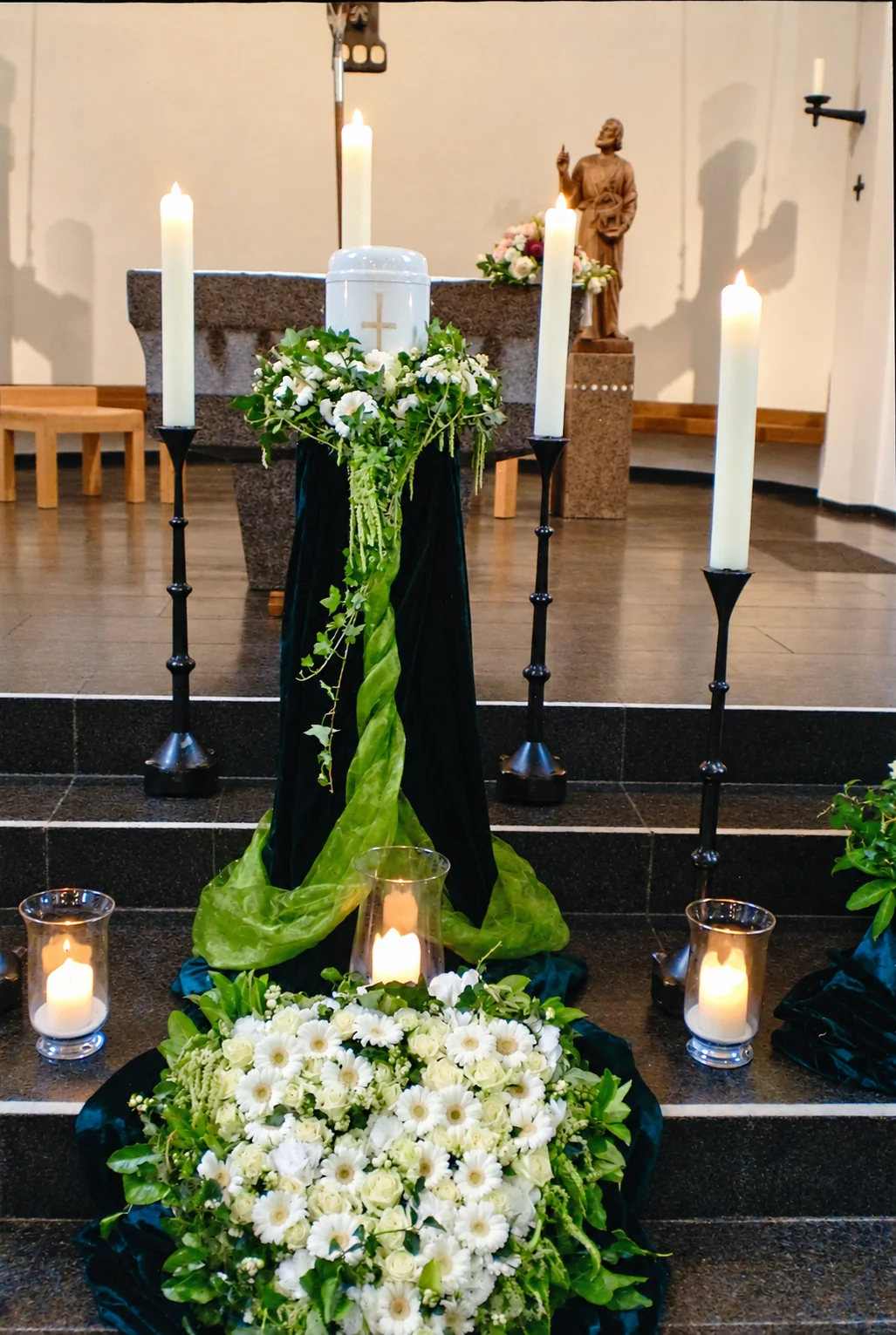 Urne mit weißem Blumenschmuck und Kerzen vor dem Altar einer Kirche, Trauerfeier von Bestattungen Lauff