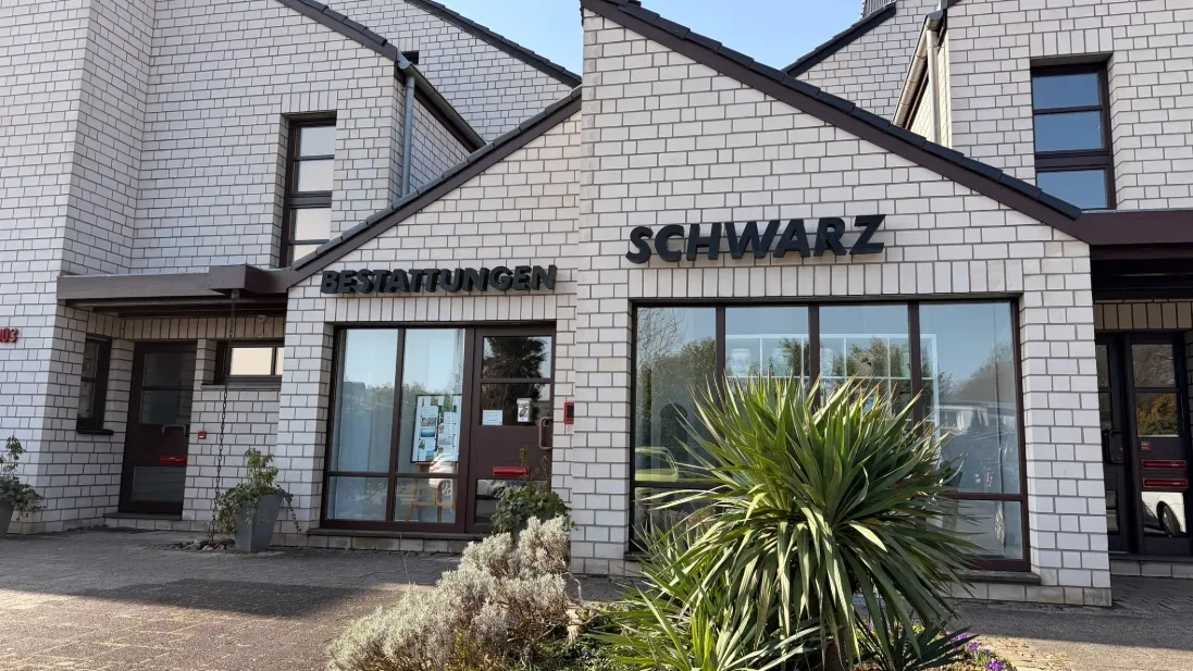 Eingang von Bestattungen Schwarz in Köln-Heimersdorf mit dem Schriftzug über der Tür und einer großen Pflanze