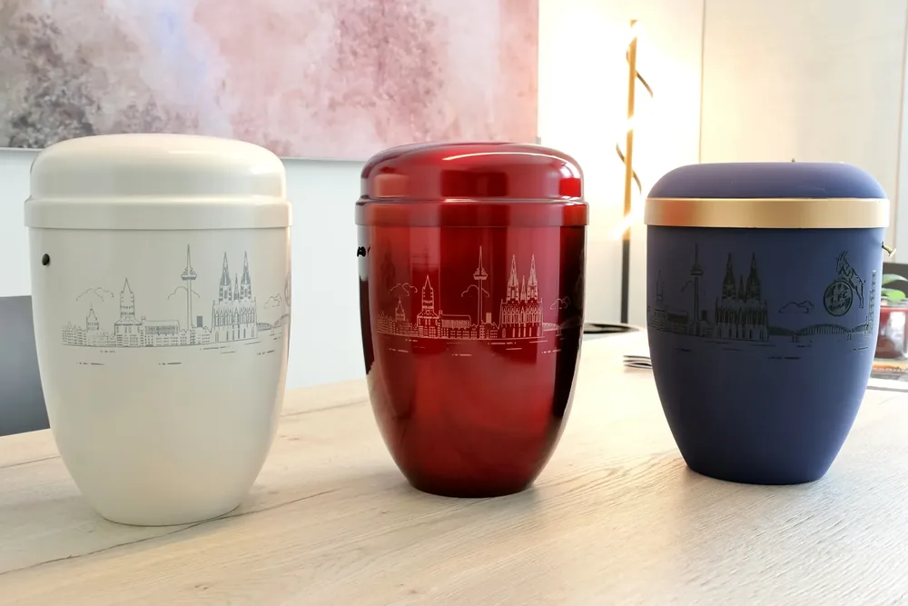 Weiße, rote und blaue Urne mit der Kölner Skyline in der Urnenausstellung von Bestattungen Schwarz