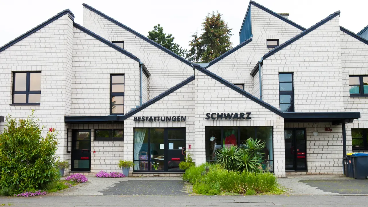 Das weiße Geschäftshaus von Bestattungen Schwarz in Köln-Heimersdorf mit bepflanztem Vorplatz