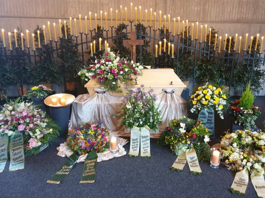 Trauerfeier mit zahlreichen bunten Blumenkränzen und vielen brennenden Kerzen