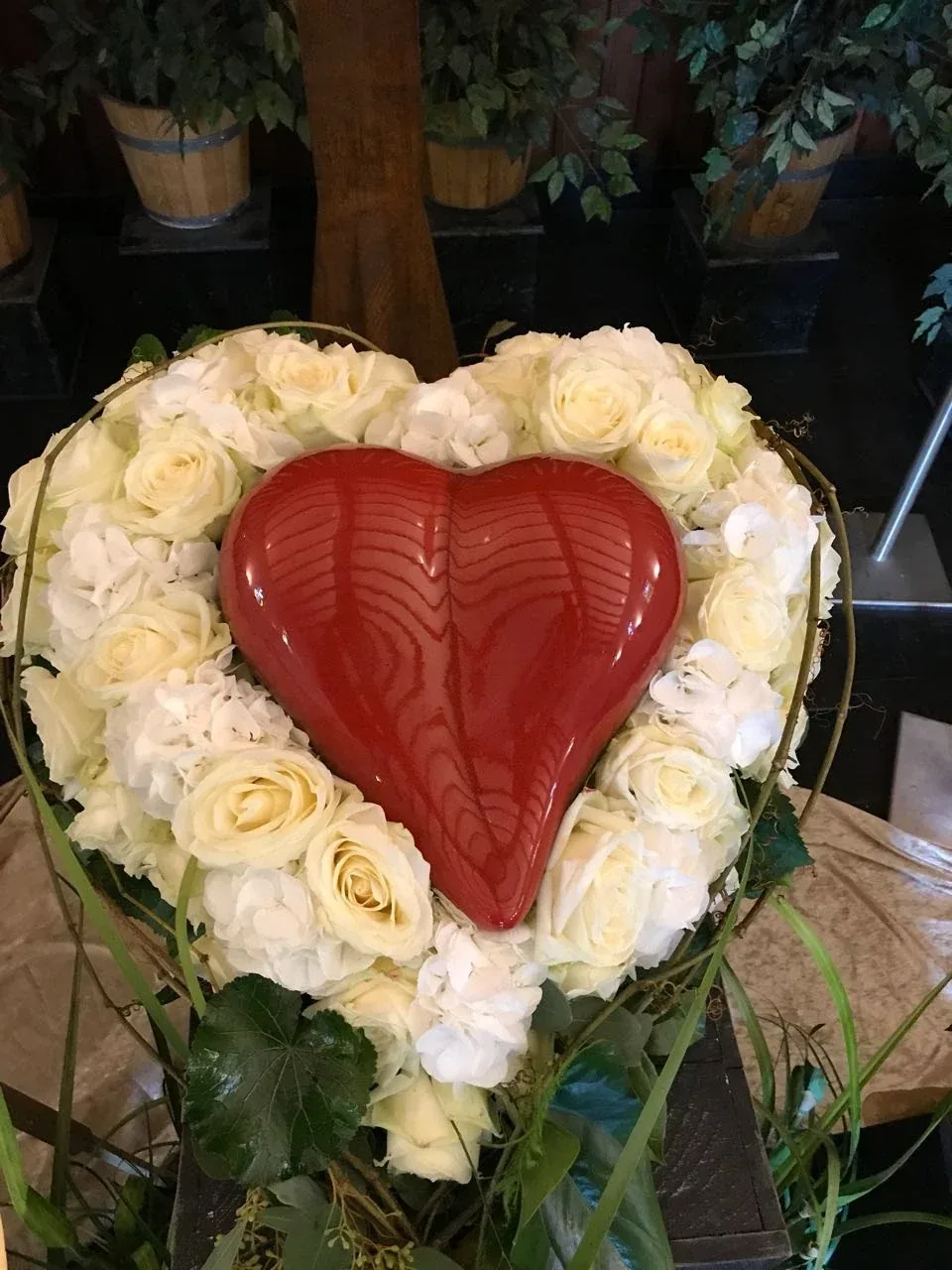 Herzförmiges Trauergesteck aus weißen Rosen mit einem roten Herz in der Mitte