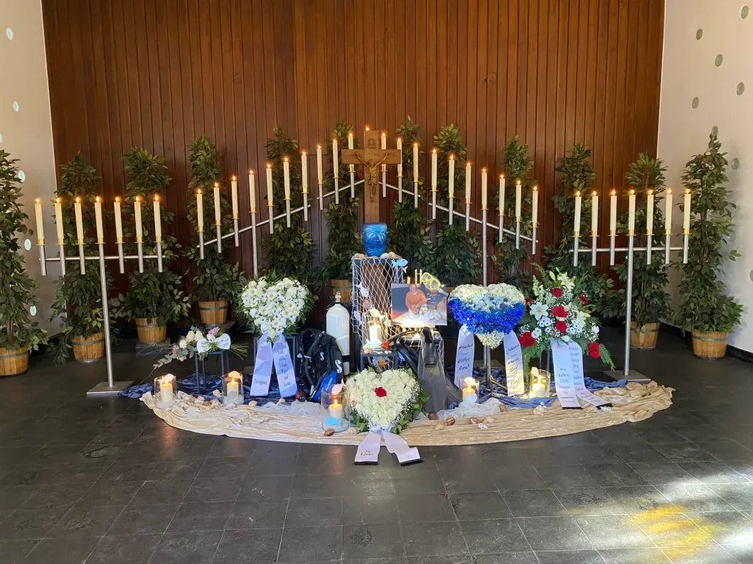 Urnenfeier mit blauer Urne, blau-weißen Blumen, Kerzen und einer Dekoration mit Meeresmotiven